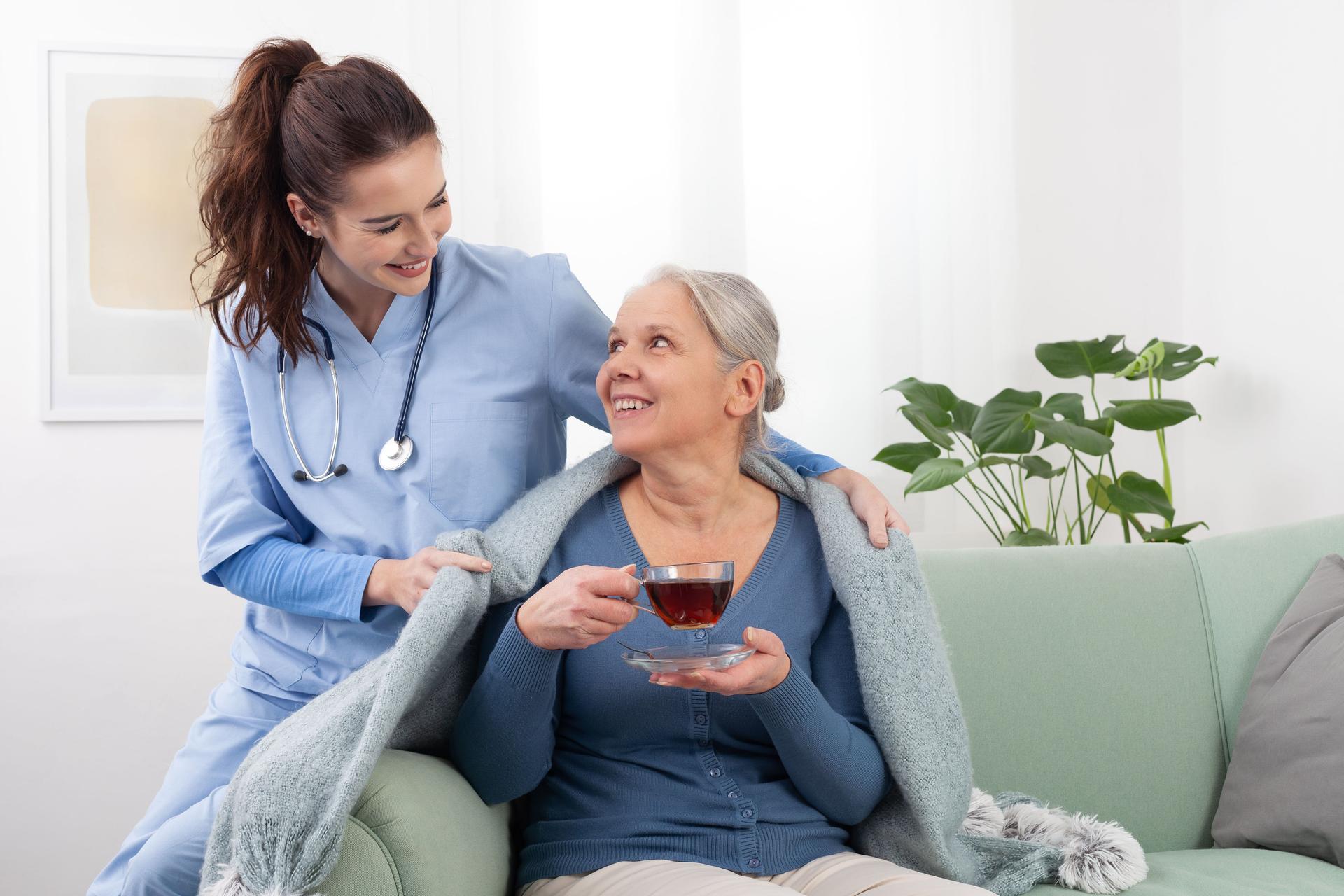 Young woman friendly nurse or doctor caregiver smiles while caring to an elderly senior woman patient. Nursing at home, in a medical clinic, or in hospice care. Concept of healthcare and insurance